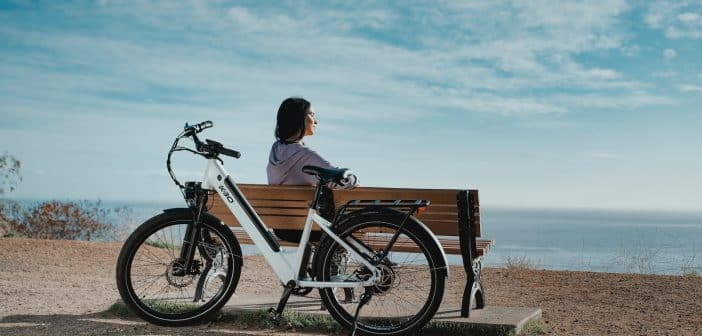 man in black shirt sitting on brown wooden bench beside black and white bicycle during daytime