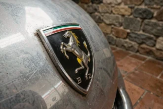 Gros plan macro sur le badge cheval cabré Ferrari, emblème iconique sur carrosserie vintage en aluminium poli dans un garage italien