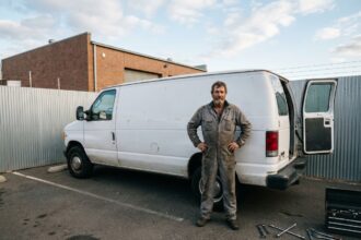 Mécanicien homme debout à côté d'une camionnette blanche dans un parking